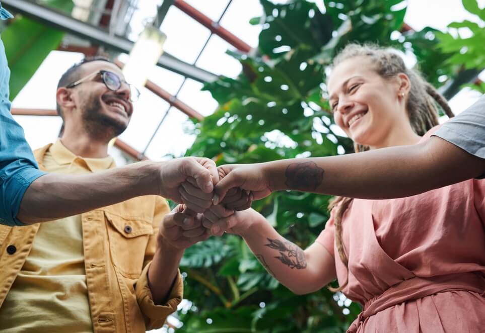 This image shows a group of four people putting their fists together in a circle and smiling at each other, showing a spirit of teamwork and collaboration.